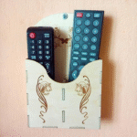 Laser-cut plywood wall-mounted holder with decorative floral pattern holding two TV remotes